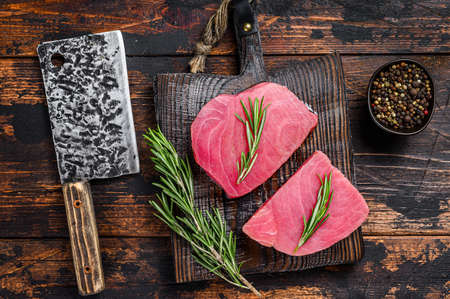 Raw tuna steaks on a wooden cutting Board with cleaver. Dark wooden background. Top view.の写真素材