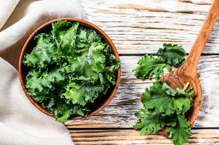 Fresh green superfood kale leaves in wooden bowl. Organic Vegetarian food. White background. Top...