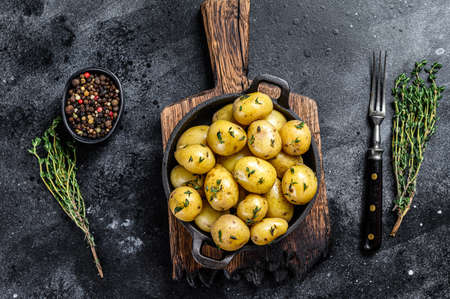 Young baby boiled potato with butter in a pan. Black background. Top view.の写真素材