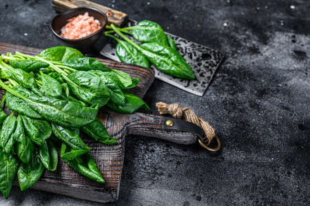 Raw fresh young baby spinach leaves on a wooden cutting board. Black background. Top view. Copy...