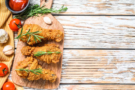 Fried crispy chicken legs, drumstick on a cutting board. White wooden background. Top view. Copy space.の写真素材