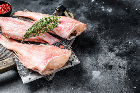 Raw Red perch or seabass fish on a cutting board. Black background. Top view. Copy space.