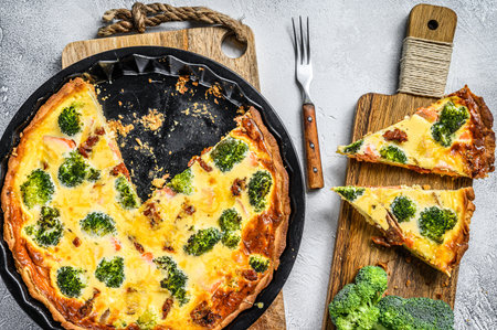 Sliced tart with salmon, broccoli and cream on a wooden cutting board. White background. Top view.の写真素材