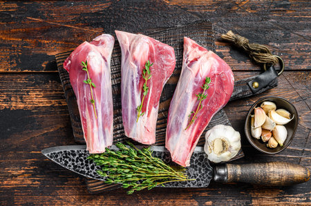 Raw lamb shanks meat on a cutting board with herbs. Dark wooden background. Top view.の写真素材
