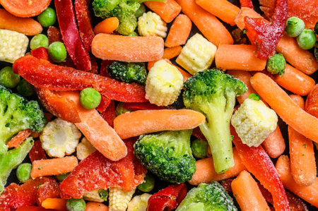 Frozen cold sliced Vegetables, broccoli, sweet peppers, tomatoes, carrots, peas and corn. Black background. top view.の写真素材