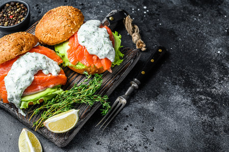 Fish burger with salted salmon, avocado, mustard sauce, cucumber and Iceberg salad. Black background. top view. Copy space.の写真素材