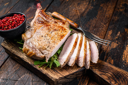 Grilled and sliced tomahawk pork chop meat steak on a marble board. Dark Wooden background. Top view.の写真素材