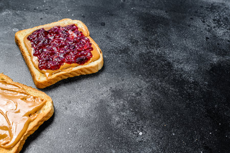 Peanut butter and jelly on white bread toasts. Black background. Top view. Copy space.の写真素材
