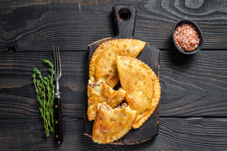 Cheburek meat pastry pie with herbs. Black wooden background. Top view.