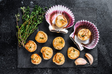 Fried seafood scallops meat with butter in a shells. Black background. Top view.の写真素材