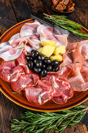 Italian meat platter with prosciutto ham, bresaola, pancetta, salami and parmesan. Dark wooden background. Top view.の写真素材