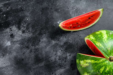 Red ripe watermelon with cut-out slices. Black background. Top view. Copy spaceの写真素材