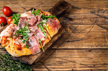 Sliced pizza with prosciutto parma ham, arugula and parmesan cheese on a wooden board. wooden background. Top view. Copy spaceの写真素材