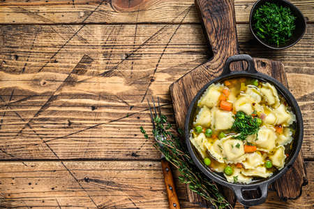 Broth soup with ravioli dumplings pasta in a pan. Wooden background. Top view. Copy spaceの写真素材