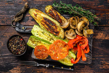 Grilled vegetables bell pepper, zucchini, eggplant and tomato with dry herbs on a wooden board. Dark wooden background. Top viewの写真素材