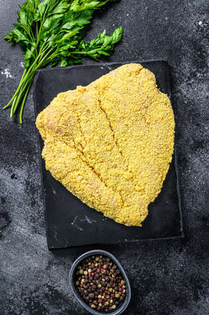 Raw large Viennese schnitzel on a cutting board. Black background. Top viewの写真素材