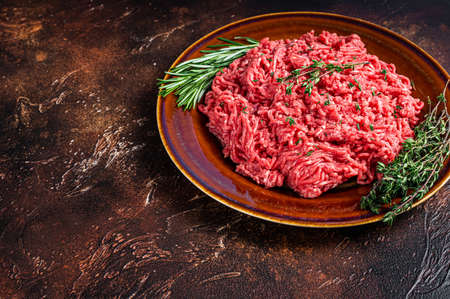 Raw ground beef or veal meat on a rustic plate with herbs. Dark background. Top view. Copy space