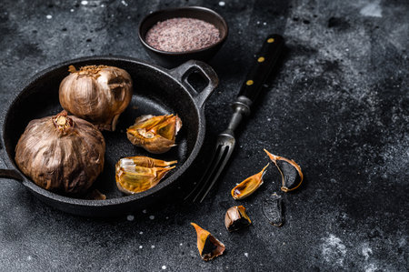 Bulbs of fermented black garlic in a pan. Black background. Top view. Copy spaceの写真素材
