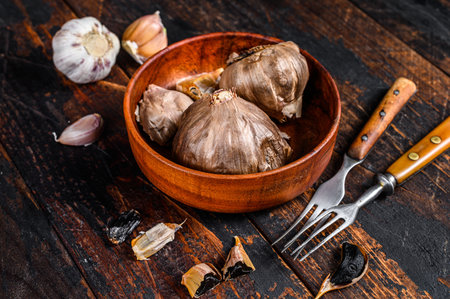 Bulbs and cloves of fermented black garlic in a plate. Dark wooden background. Top viewの写真素材