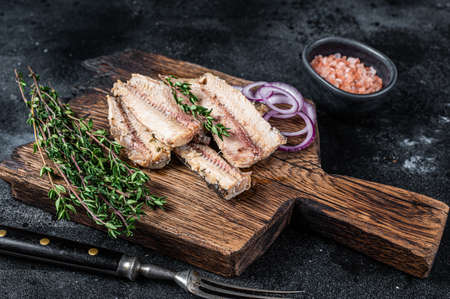 Sardine fish fillet in olive oil on wooden board. Black background. Top view