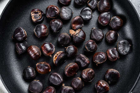 Roast chestnuts in a pan on a wooden table. White background. Top viewの写真素材