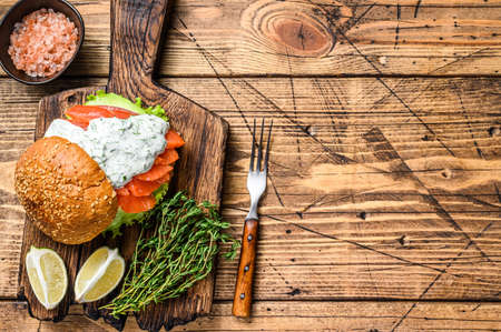 Sandwich with salted fish salmon, avocado, burger bun, mustard sauce and Iceberg salad. wooden background. top view. Copy spaceの写真素材