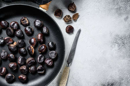 Roast chestnuts in a pan on a wooden table. White background. Top view. Copy spaceの写真素材