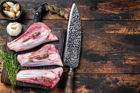 Raw veal shanks meat on a cutting board with herbs. Dark wooden background. Top view. Copy spaceの写真素材