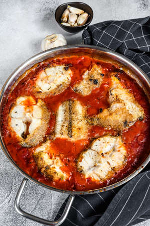 Baked grenadier macrurus white fish with tomato in a pan. White Wooden background. Top view