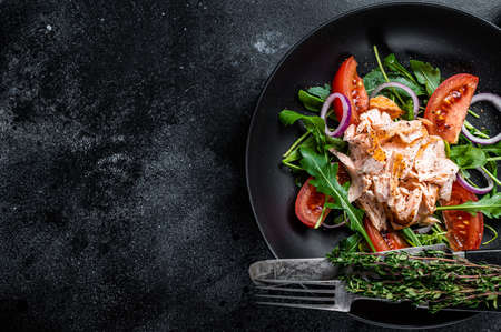 Salad with baked salmon fillet steak, fresh arugula and tomato in a plate. Black background. Top view. Copy spaceの写真素材