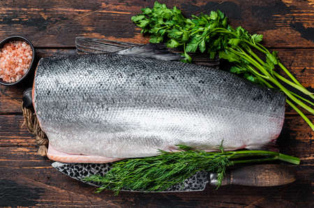 Big piece of Raw cut salmon fish on a wooden cutting board with chef knife. Dark Wooden background....