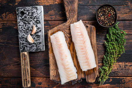 Raw cod loin fillet steak on wooden board with butcher cleaver. Dark wooden background. Top view.の写真素材