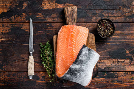 Salmon fillet fish on a wooden board with herbs and salt. Dark wooden background. Top view.の写真素材