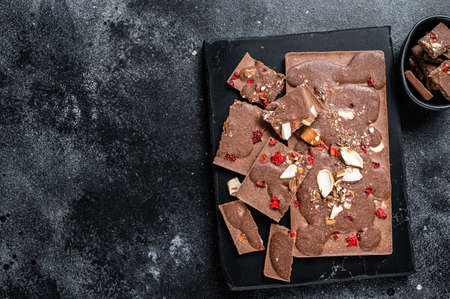 Craft homemade chocolate bars chopped on marble board. Black background. Top view. Copy space