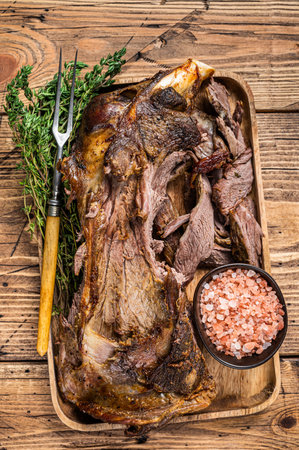 Roasted lamb mutton cutting shoulder meat in a wooden tray with meat fork. wooden background. Top viewの写真素材