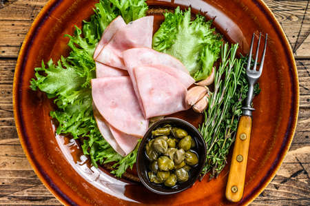Sliced smoked ham with fresh salad and capers on a plate. wooden background. Top viewの写真素材