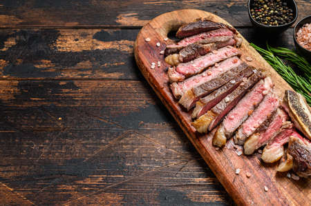 Grilled cowboy or rib eye beef steak with herbs and spices. Wooden dark background. Top view. Copy spaceの写真素材