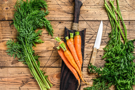 Orange carrots with leaves on a cutting board. Wooden background. Top viewの写真素材