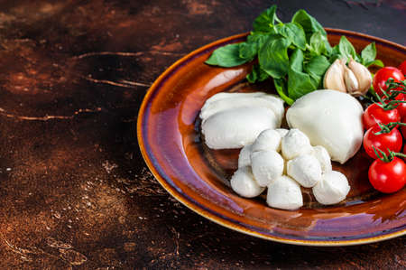 Mozzarella cheese, basil and tomato cherry ready for cooking Caprese salad. Dark background. Top...