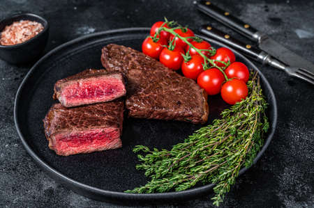Roasted cut denver beef meat steak on a plate with thyme. Black background. Top viewの写真素材