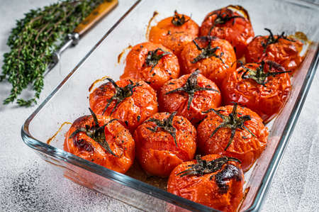 Baked cherry tomatoes with olive oil and thyme in baking dish. White background. Top viewの写真素材