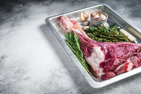 Uncooked Raw goat or lamb leg with herbs in baking tray. White background. Top view. Copy spaceの写真素材