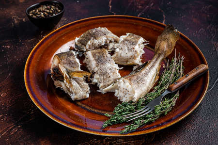 Baked cod white fish in a plate. Dark wooden background. Top view