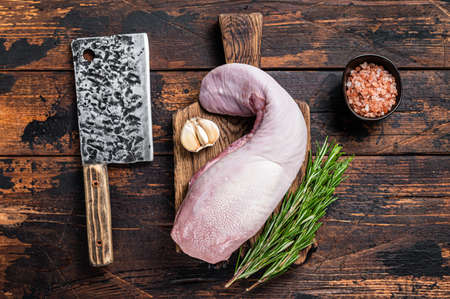 Uncooked Raw beef or veal tongue on butcher board with meat cleaver. Dark wooden background. Top viewの写真素材