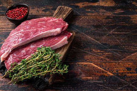 Raw top sirloin cap steak or Picanha steak on wooden board with thyme. Dark wooden background. Top view. Copy spaceの写真素材