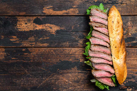 Grilled baguette steak sandwich with arugula and cheese. Dark wooden background. Top view. Copy spaceの写真素材