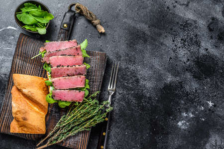 Baguette Tuna steak sandwich with arugula on a cutting board. Black background. Top view. Copy spaceの写真素材