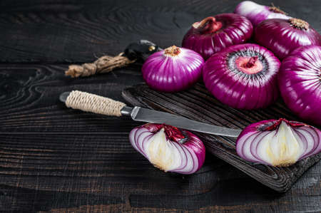 Whole and halfed Flat red sweet onion on a cutting board. Black Wooden background. Top View. Copy...