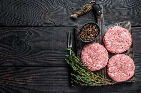 Raw chicken turkey patty, ground meat cutlets on a chopping Board. Black wooden background. Top view. Copy spaceの写真素材