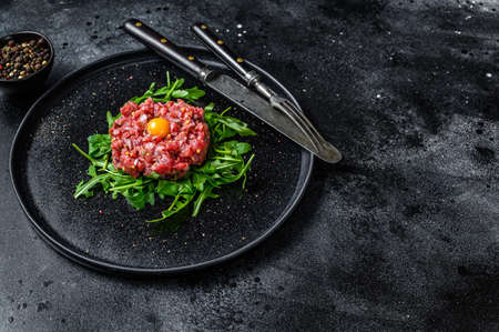 Beef tartar with a quail egg served on a black stone plate.. Black background. Top view. Copy spaceの写真素材